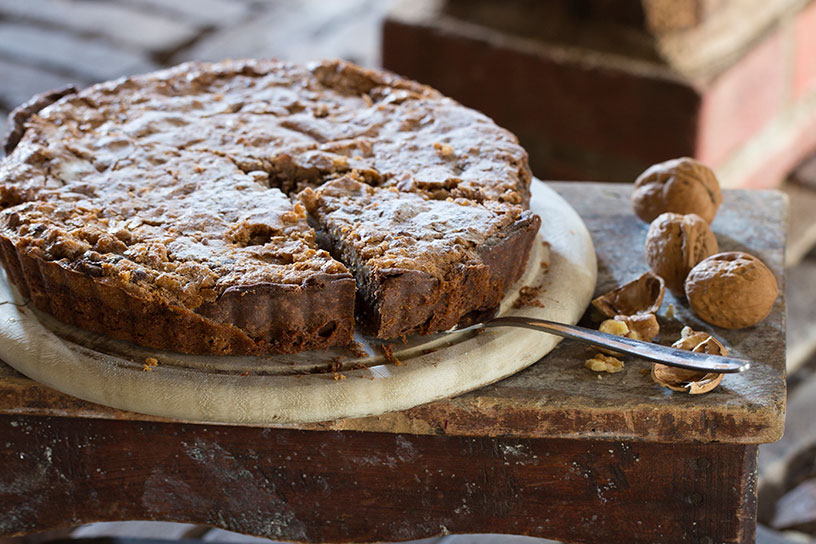 Een aangesneden walnotentaart met losse walnoten ernaast